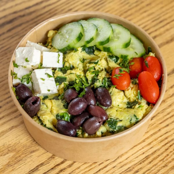 Scrambled eggs with spinach, feta, olives, cherry tomatoes, and cucumber slices in a bowl.