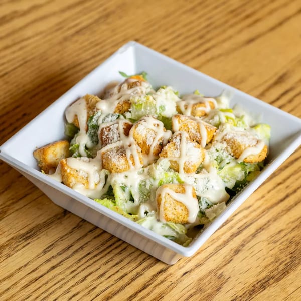 Caesar salad with croutons, dressing, and grated cheese in a white bowl on a wooden table.