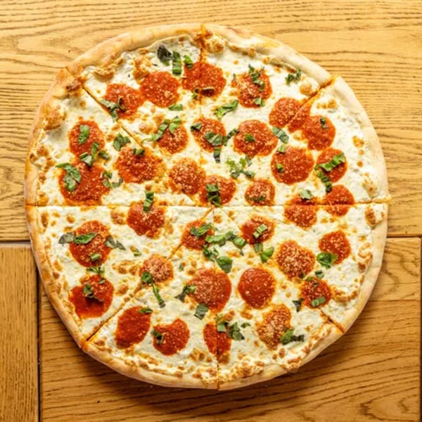 A white pizza with dollops of red sauce, fresh basil, and parmesan cheese on a wooden table.