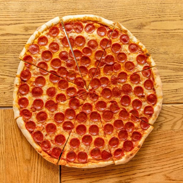 A whole pepperoni pizza, cut into slices, rests on a light brown wooden table.