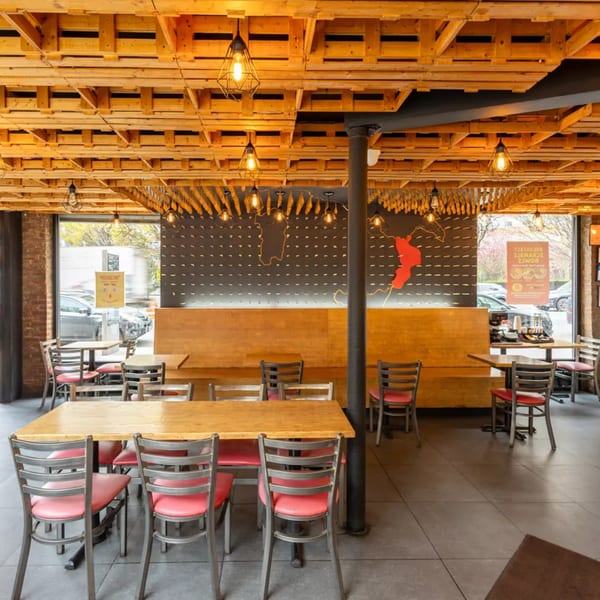 Restaurant interior with wooden pallet ceiling, industrial pendant lights, red-seated chairs, and wooden tables.