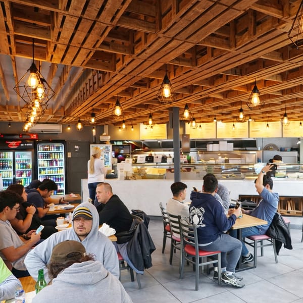Customers seated at tables in a brightly lit restaurant with a wooden slatted ceiling and counter service.