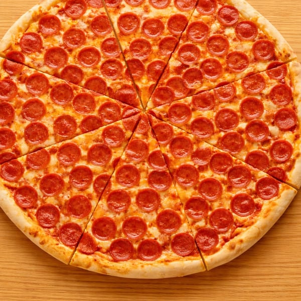 A whole pepperoni pizza, cut into many slices, sits on a light wooden table.