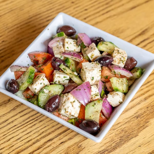 A fresh Greek salad with feta, olives, red onion, tomatoes, and cucumbers in a white bowl.