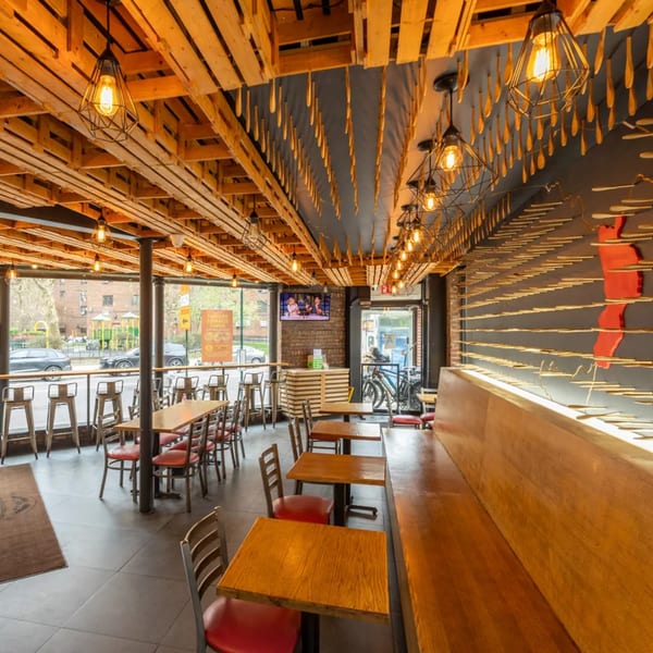 Restaurant interior with wooden tables, red chairs, a long wooden bench, and unique ceiling decor.