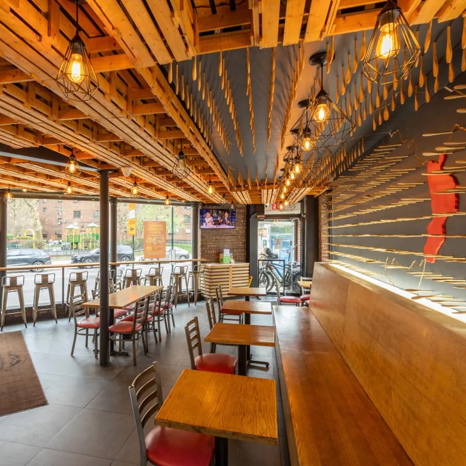 Restaurant interior with wooden tables, red chairs, a long wooden bench, and unique ceiling decor.