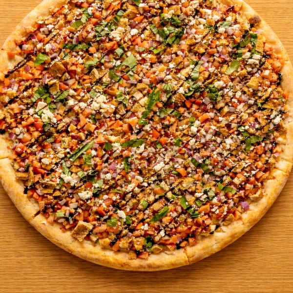 A whole pizza topped with diced tomatoes, chicken, red onion, feta, basil, and balsamic glaze.
