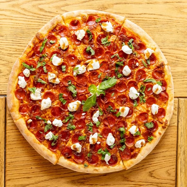 Pepperoni pizza with dollops of ricotta cheese and fresh basil on a wooden table.