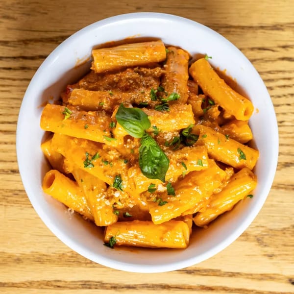 Rigatoni pasta in a creamy orange sauce, topped with fresh basil and parsley, in a white bowl.