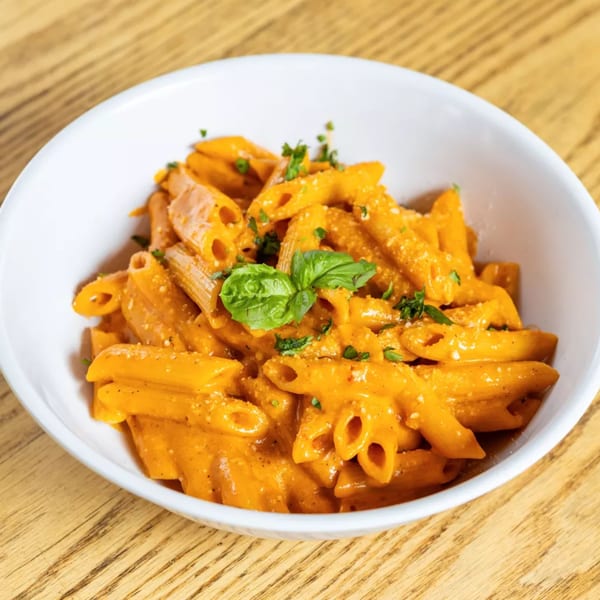 Penne pasta in a creamy orange sauce, garnished with fresh basil and parsley in a white bowl.